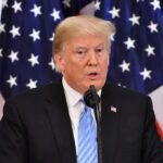 A man speaking at a podium with American flags in the background