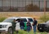 California Border Crackdown Returns law enforcement officers confer beside patrol vehicles near a border fence