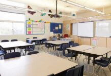 Teacher Under Fire Over Alleged Period Incident Empty classroom with tables, chairs, and a whiteboard