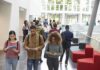 Elite College Courses Spark Ideology Debate Students walking through a bright campus atrium using mobile devices