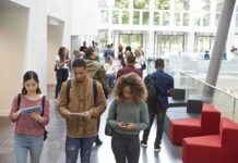 Elite College Courses Spark Ideology Debate Students walking through a bright campus atrium using mobile devices