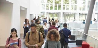 Students walking through a bright campus atrium using mobile devices