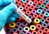 Your Blood Test Could Change With the Seasons Gloved hand holding blood vial over colorful test tubes