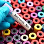 Gloved hand holding blood vial over colorful test tubes