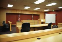 Court Clears Path to Inspect Shooter’s Writings Interior view of an empty courtroom with wooden furniture and American flags