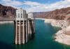 NASA Spots: Lake Powell Nears Critical Levels A large dam structure with two towers over a blue water reservoir surrounded by rocky mountains