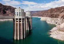 NASA Spots: Lake Powell Nears Critical Levels A large dam structure with two towers over a blue water reservoir surrounded by rocky mountains