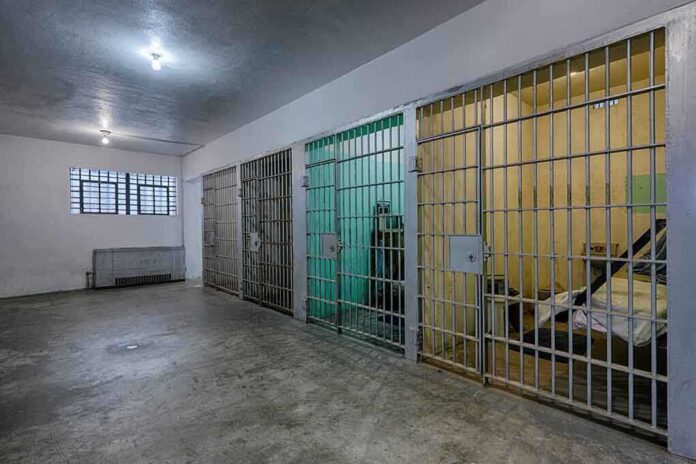 shutterstock_154636196-1 Interior view of a prison cell block with metal bars and concrete flooring
