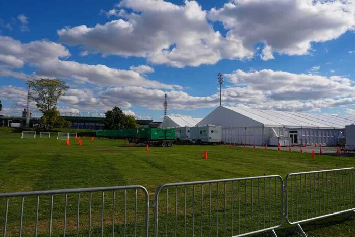 Temporary white tents and equipment on a grassy field with traffic cones and metal barriers