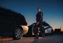 911: Fake Cop Calls Real Police Police officer standing near patrol car during twilight traffic stop