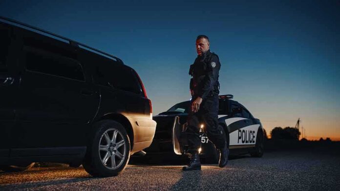shutterstock_2232055247-1 Police officer standing near patrol car during twilight traffic stop