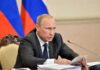 Vladimir Putin speaking at a meeting with documents and a microphone