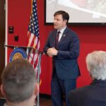 Georgia Senate Race Erupts Over Extremism Claims Speaker in a navy suit addressing an audience at a podium