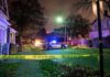 Police car blocks residential street at night behind caution tape