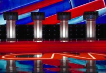 Race Bombshell Ignites California Debate Debate stage with four empty podiums and bright red and blue backdrop