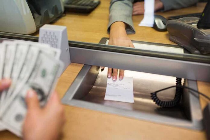shutterstock_562302346 Bank teller hands receipt through service window