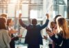 Businessman raising fists as colleagues applaud in office