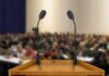Ancient Collapse Offers Modern Warning Podium with two microphones facing a blurred audience
