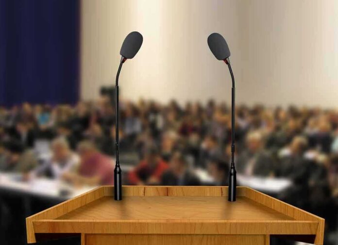 shutterstock_83211922-1 Podium with two microphones facing a blurred audience